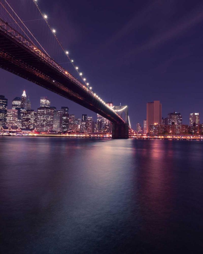 A lit suspension bridge over dark water at night.
