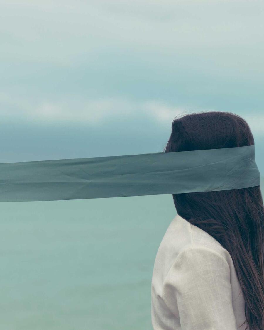 A person in a pale head covering looking out over flat water.