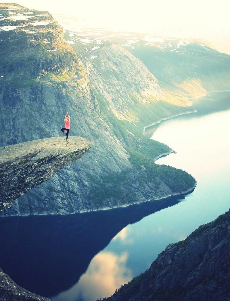 A lone walker on a rocky ledge above still water.